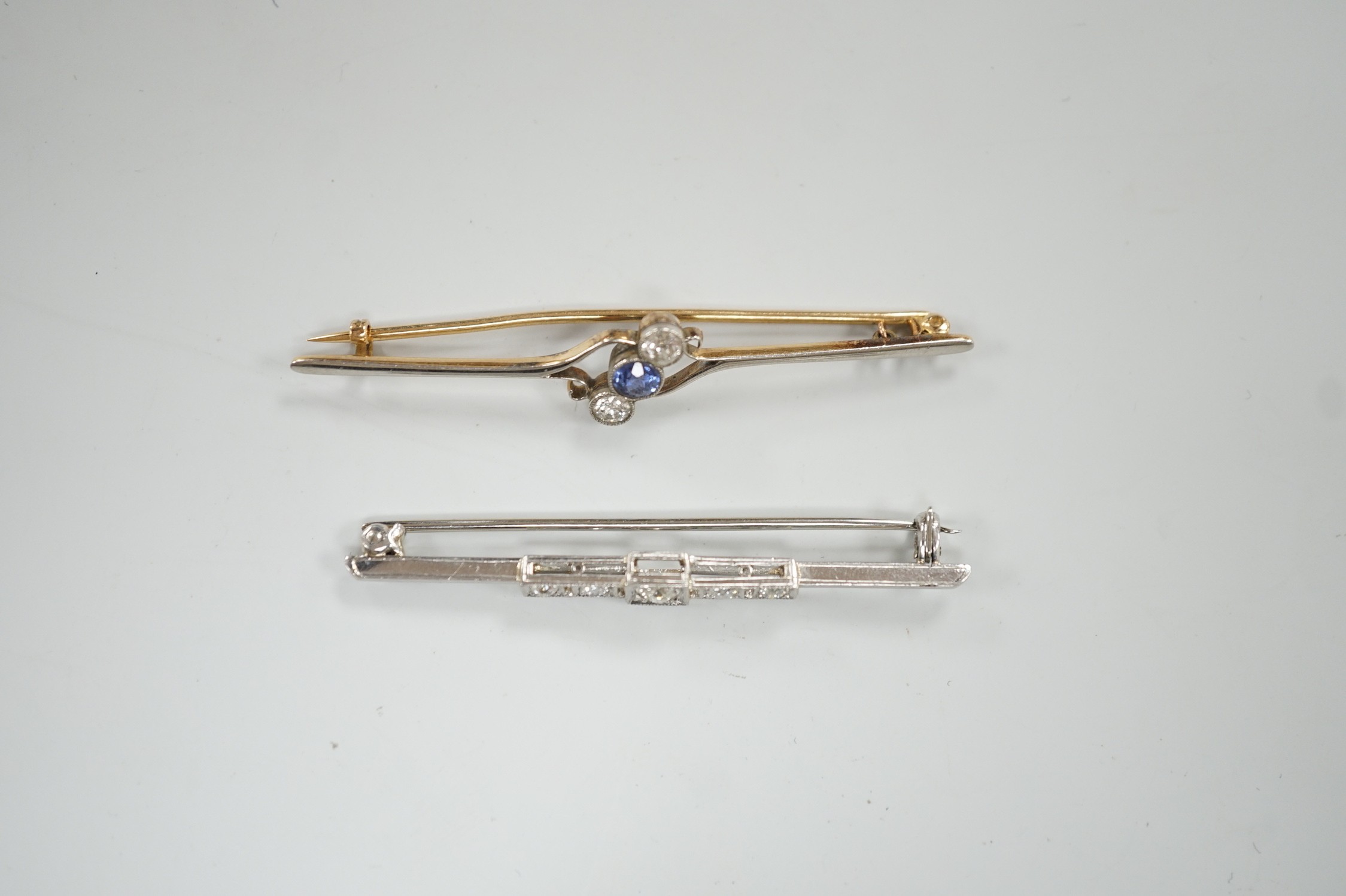 An early to mid 20th century white metal and five stone diamond set bar brooch, 50mm and a similar yellow metal, two stone diamond and single stone sapphire set crossover bar brooch, gross weight 7.1 grams.